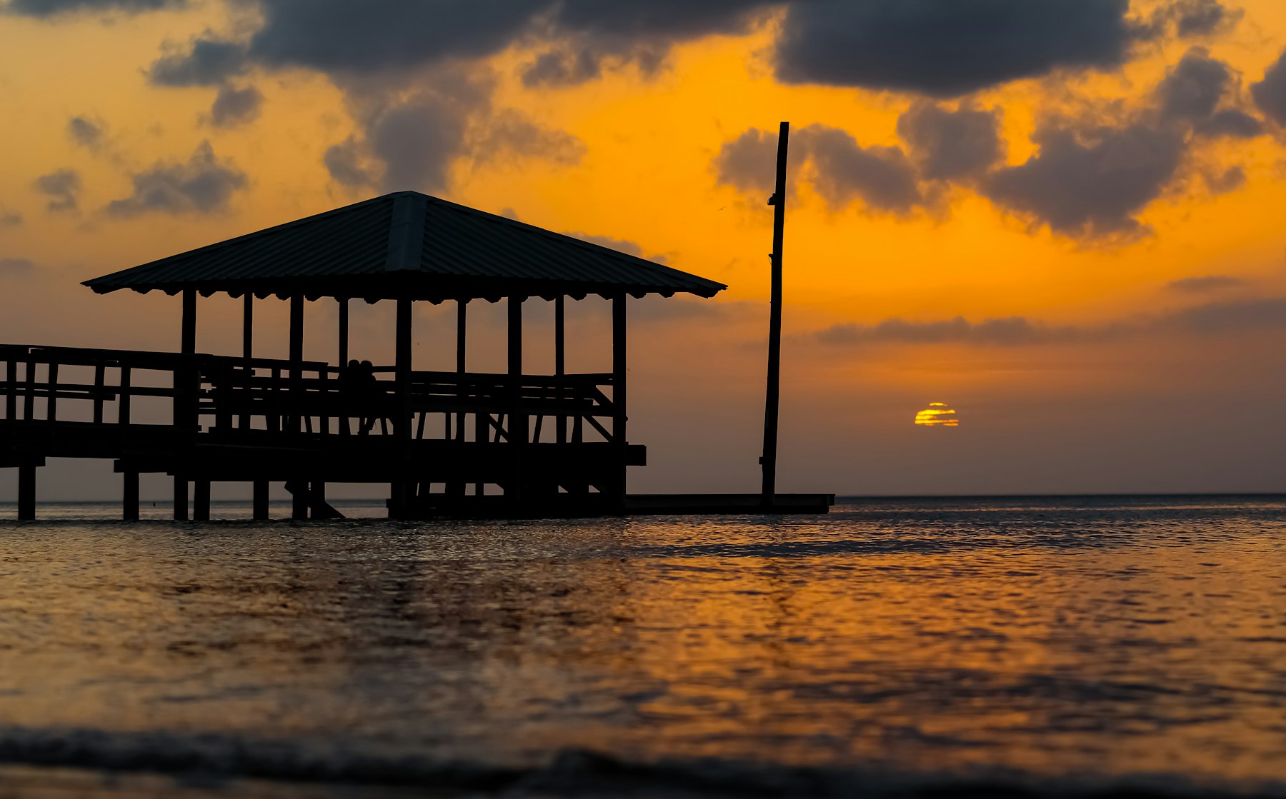 A covered pier over still water at sunset on the Mississippi coast